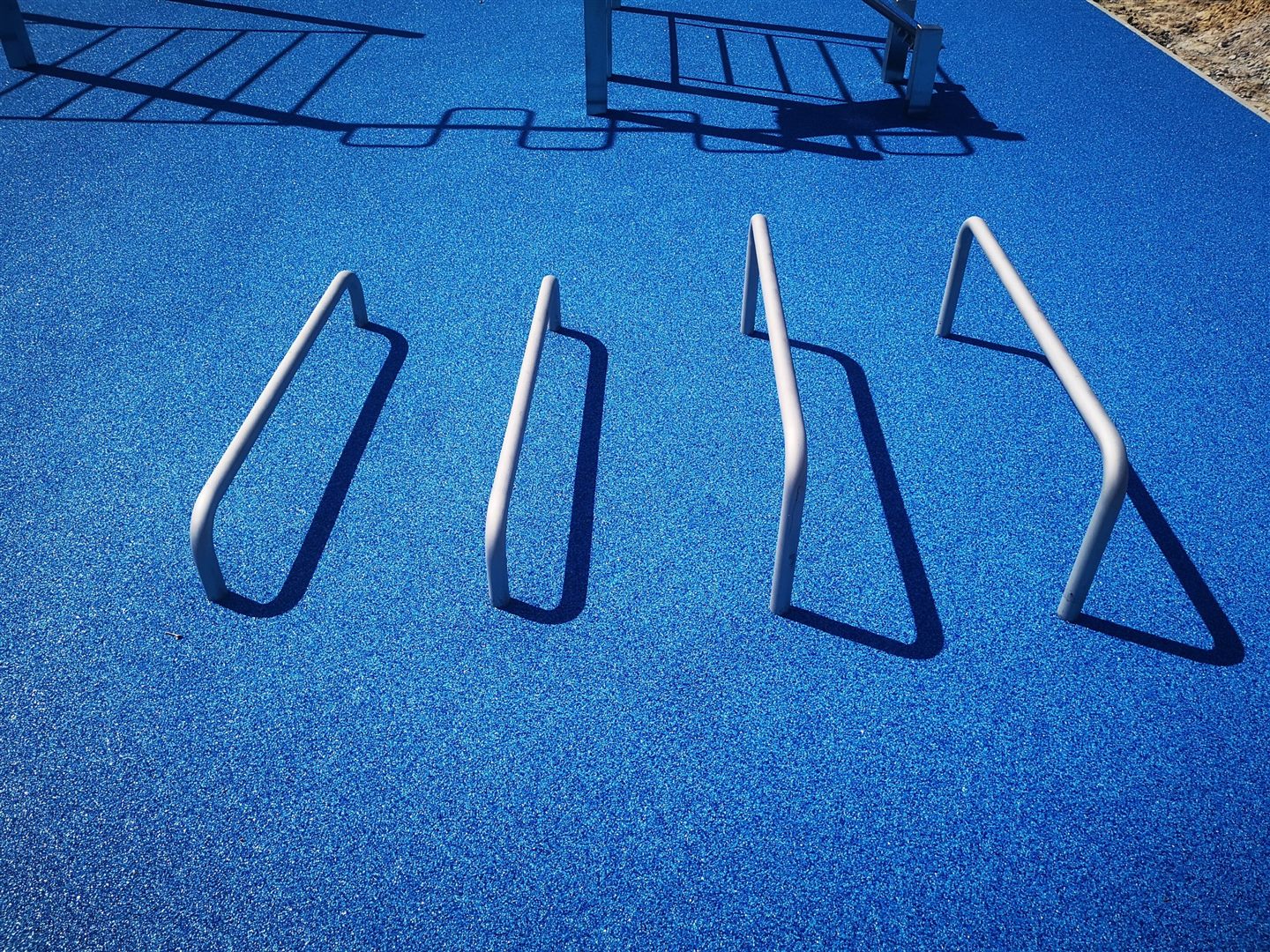 Silberne Trainingsbügel werfen lange Schatten auf einen blauen elastischen Belag.