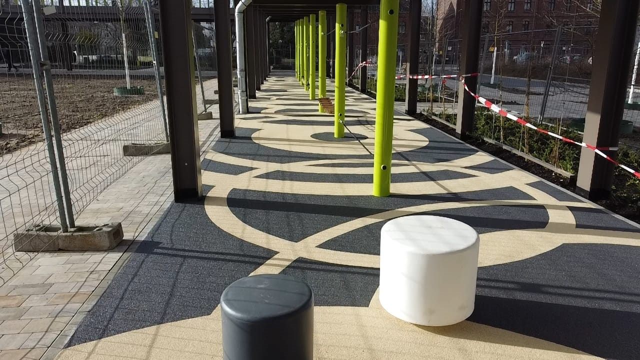 Schwarze und sandfarbene Bewegungsfläche mit gelben Trainingsstangen unter einer Brücke.
