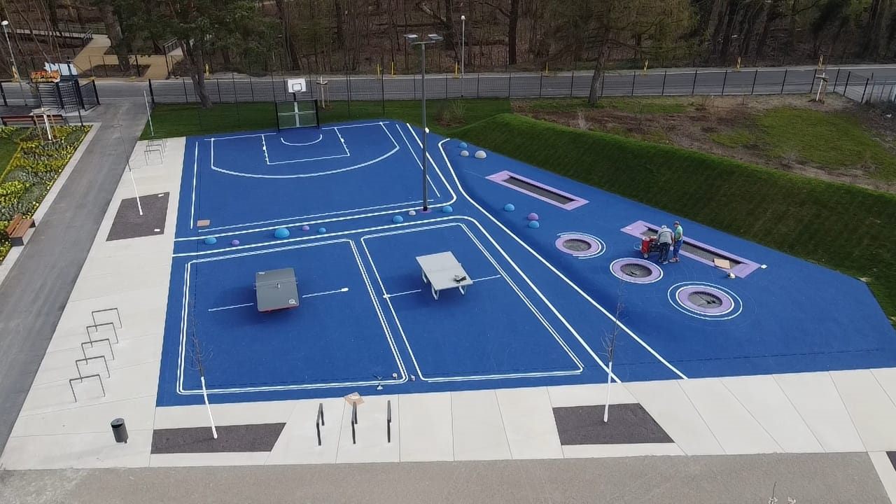 Blaues Multisportfeld mit weißen Linien und angrenzenden Bewegungszonen von oben.