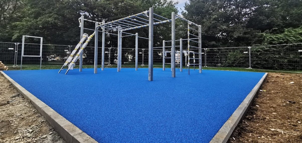 Blaue Trainingsfläche mit silbernen Calisthenics-Geräten am Waldrand.
