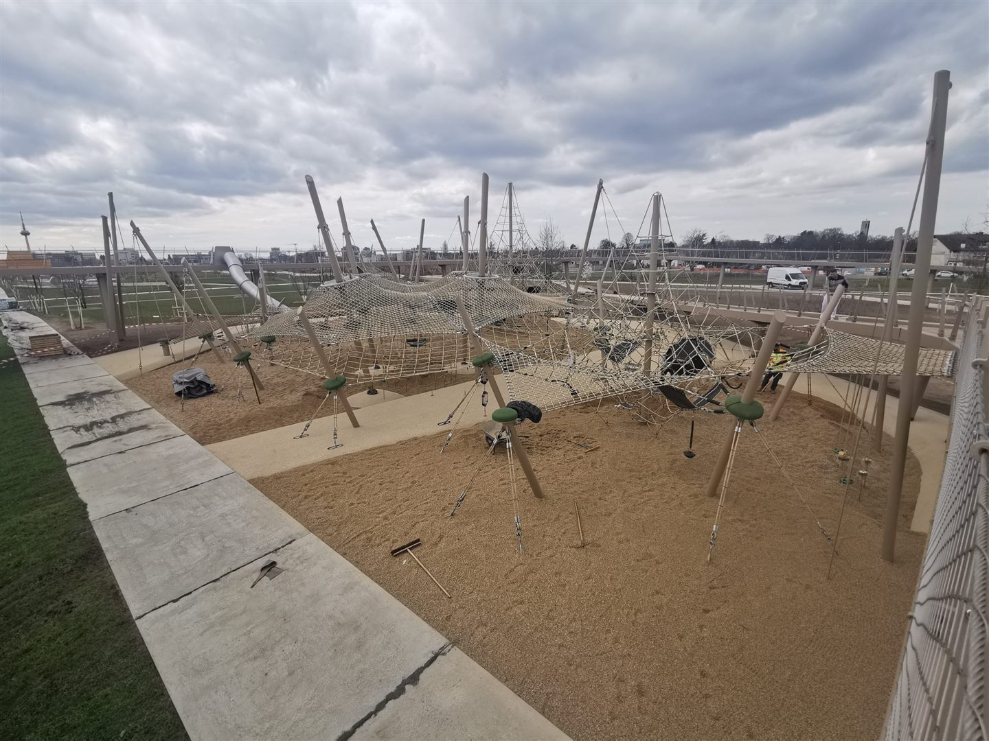 Weitläufige sandfarbene Spiellandschaft mit hohen Seil- und Klettergeräten.