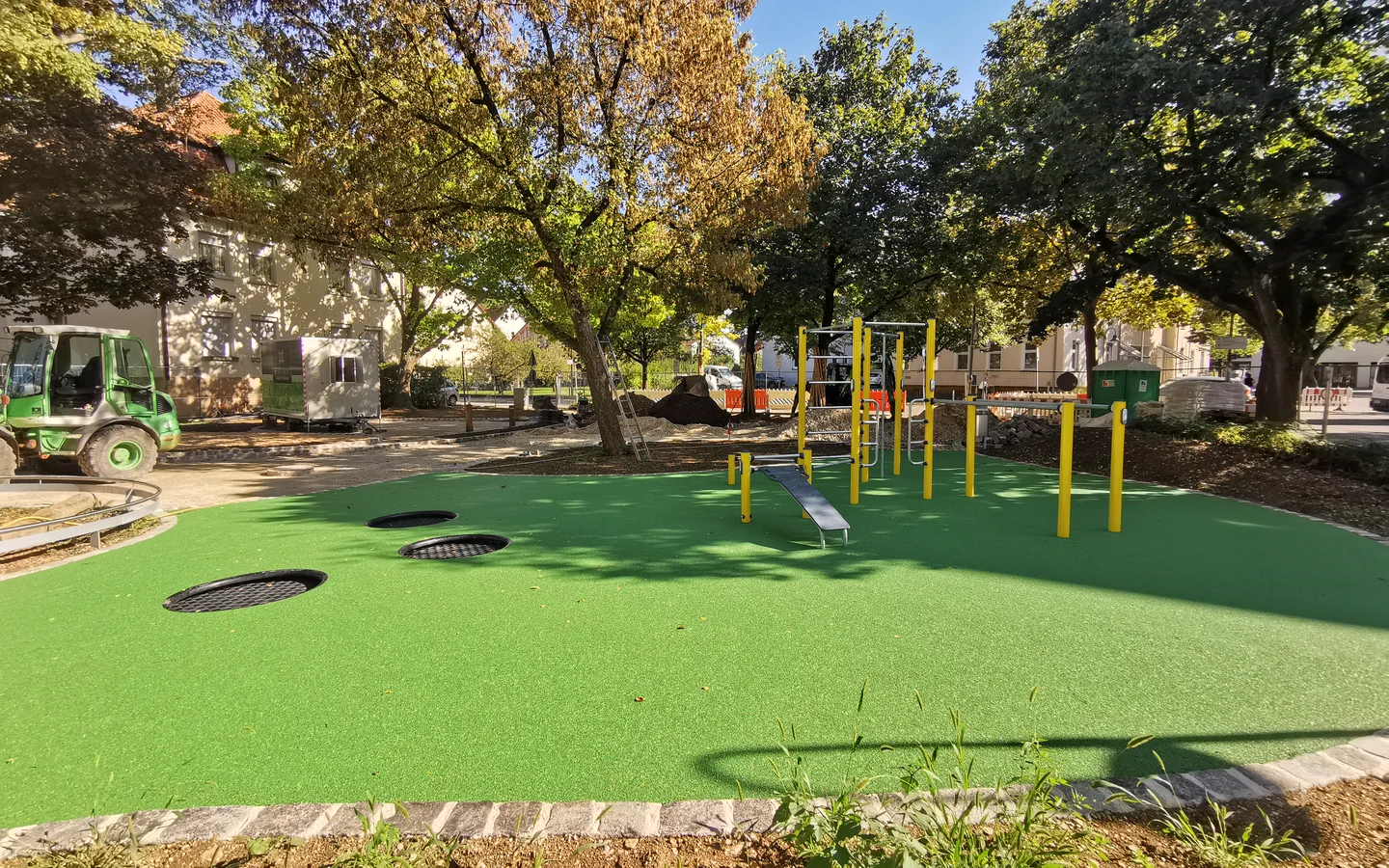 Grüne Bewegungsfläche mit Fitnessgeräten zwischen Bäumen.