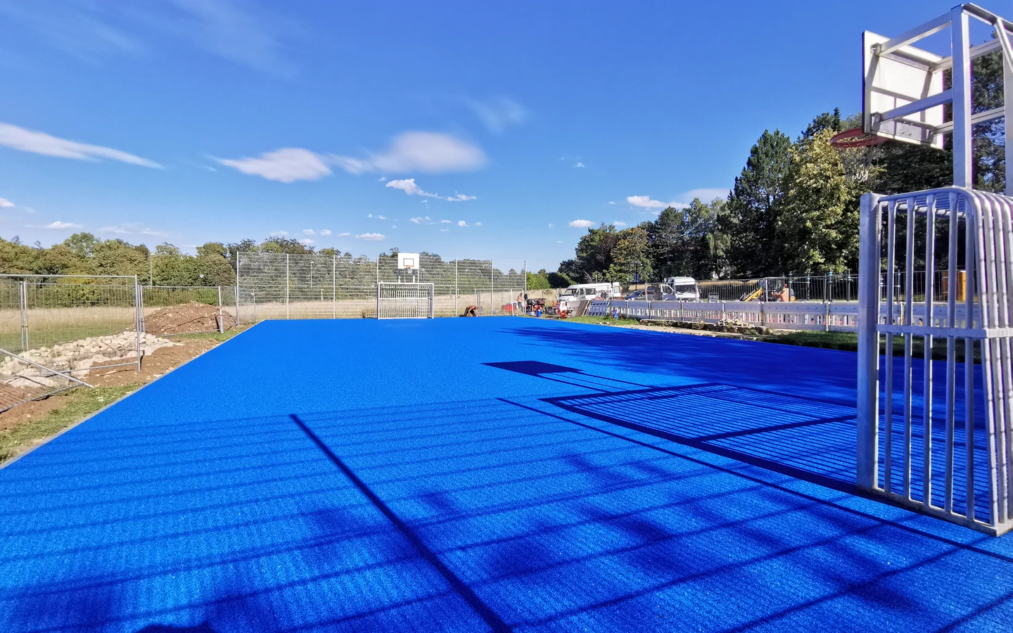 Blaue Sportfläche mit Basketballkörben und langen Schattenlinien.